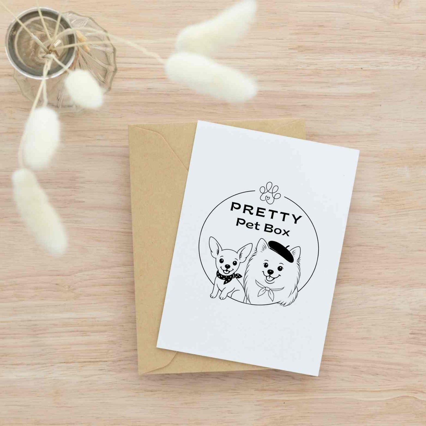 Carte illustrée Pretty Pet Box avec deux petits chiens stylisés, posée sur une enveloppe kraft sur fond bois clair – papeterie chic et naturelle pour les amoureux des petits chiens